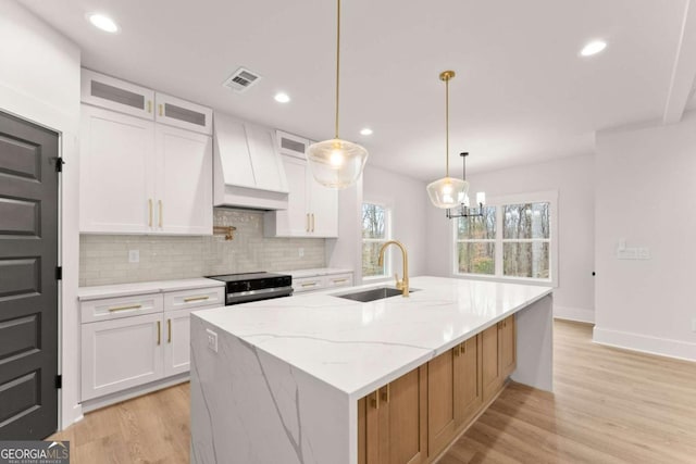 kitchen with visible vents, premium range hood, white cabinetry, a sink, and range with electric stovetop