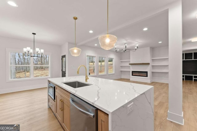 kitchen featuring light wood finished floors, a glass covered fireplace, appliances with stainless steel finishes, a sink, and recessed lighting