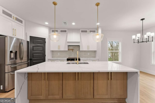 kitchen with stainless steel fridge, a spacious island, backsplash, white cabinetry, and a sink