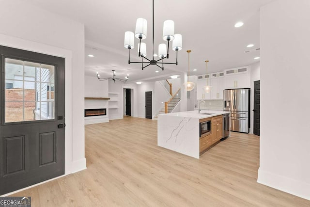 kitchen featuring light wood finished floors, a glass covered fireplace, stainless steel appliances, white cabinetry, and a sink