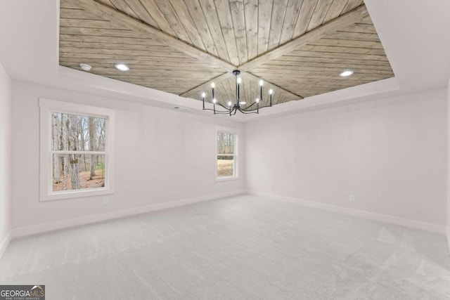 carpeted spare room featuring a chandelier, wooden ceiling, a raised ceiling, and baseboards