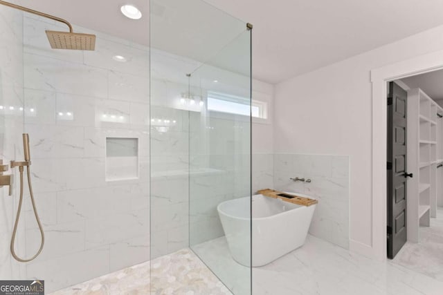 bathroom with marble finish floor, a freestanding tub, a marble finish shower, and tile walls