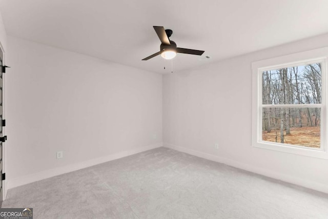 empty room featuring a ceiling fan, light colored carpet, and baseboards