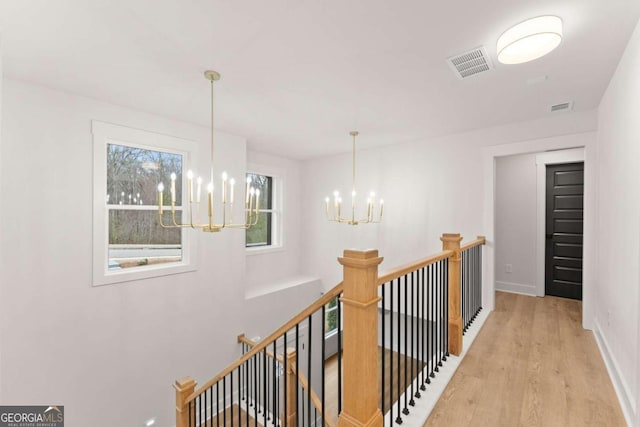 corridor featuring an inviting chandelier, light wood-style flooring, visible vents, and an upstairs landing