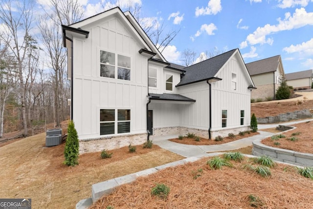 exterior space featuring board and batten siding, central AC, a shingled roof, and brick siding