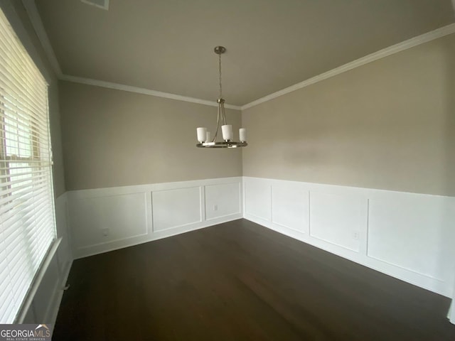 unfurnished dining area featuring a wainscoted wall, ornamental molding, dark wood-type flooring, and a notable chandelier