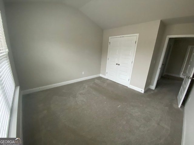 unfurnished bedroom with vaulted ceiling, dark colored carpet, and baseboards