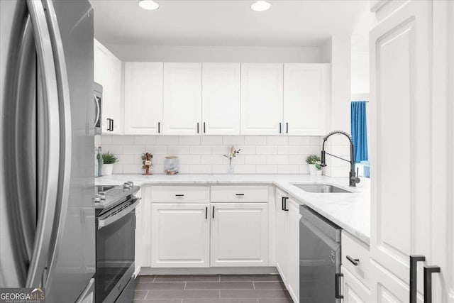 kitchen with appliances with stainless steel finishes, white cabinets, a sink, and tasteful backsplash