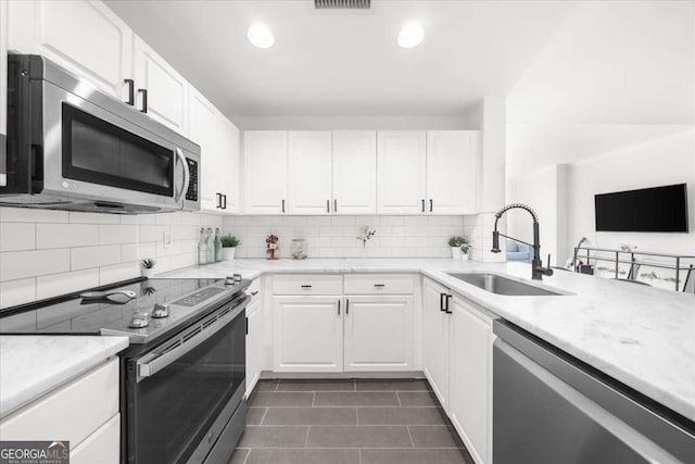 kitchen featuring tasteful backsplash, appliances with stainless steel finishes, white cabinetry, a sink, and dark tile patterned flooring