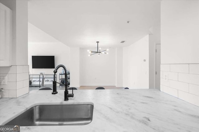 kitchen with backsplash, open floor plan, a sink, light stone countertops, and a notable chandelier