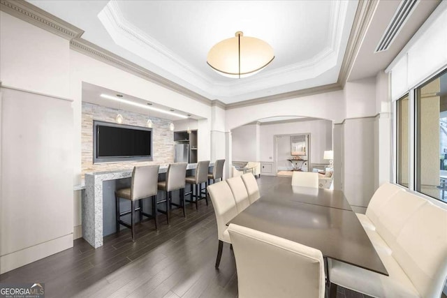 dining room with ornamental molding, arched walkways, a raised ceiling, and wood finished floors