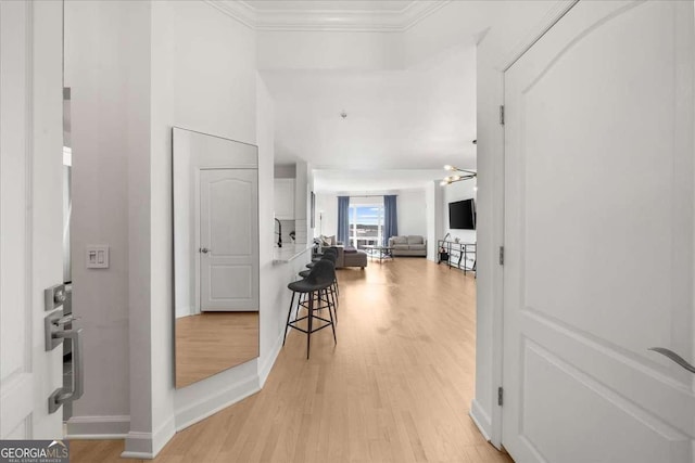 hallway with light wood-style flooring, baseboards, and crown molding