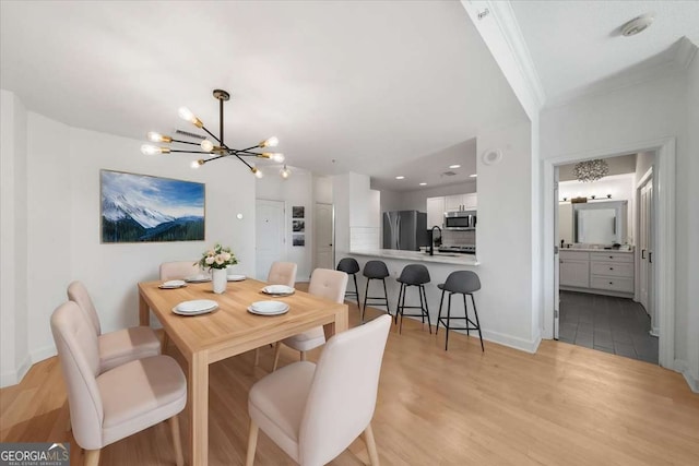 dining room featuring a chandelier, ornamental molding, light wood-style flooring, and baseboards