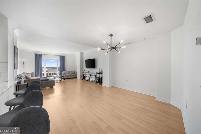 living room featuring baseboards, light wood-style flooring, visible vents, and a notable chandelier