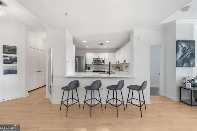 kitchen featuring stainless steel appliances, white cabinetry, light wood-style floors, and tasteful backsplash