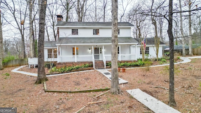 view of front of house with a porch, a chimney, and fence