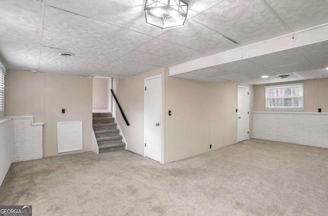 basement featuring brick wall, carpet, and stairway