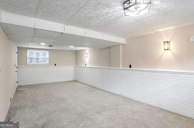 basement with carpet flooring, a drop ceiling, and brick wall