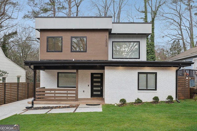 modern home with covered porch, fence, a front lawn, and brick siding