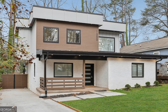 modern home with a front yard, a porch, board and batten siding, and brick siding