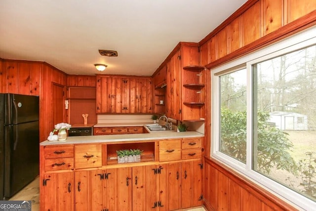 kitchen with a sink, light countertops, freestanding refrigerator, brown cabinets, and open shelves