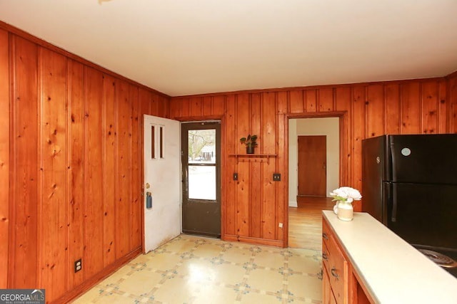 kitchen featuring light floors, brown cabinets, freestanding refrigerator, and wooden walls