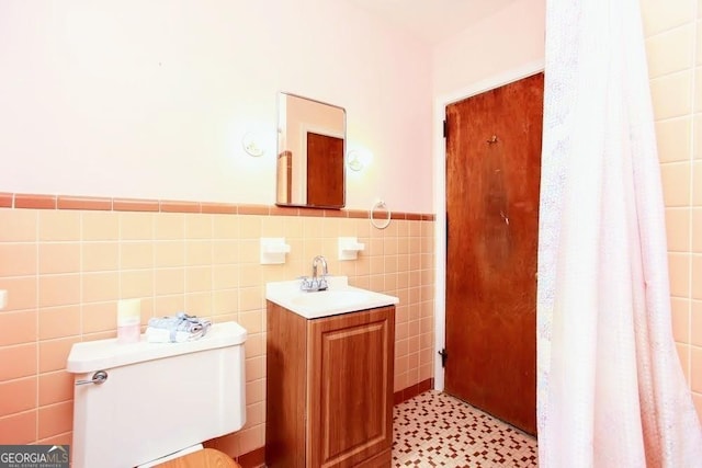 bathroom with toilet, wainscoting, tile walls, and vanity