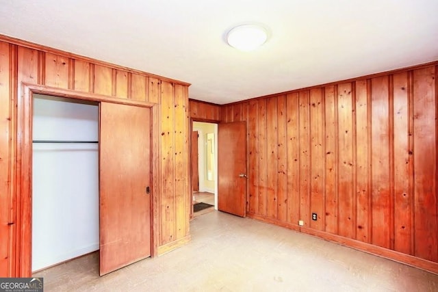 unfurnished bedroom featuring a closet, baseboards, wood walls, and light floors