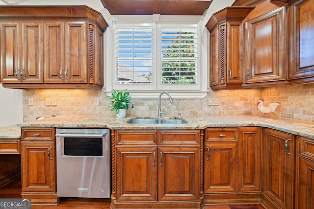 kitchen featuring brown cabinetry, backsplash, a sink, light stone countertops, and stainless steel dishwasher