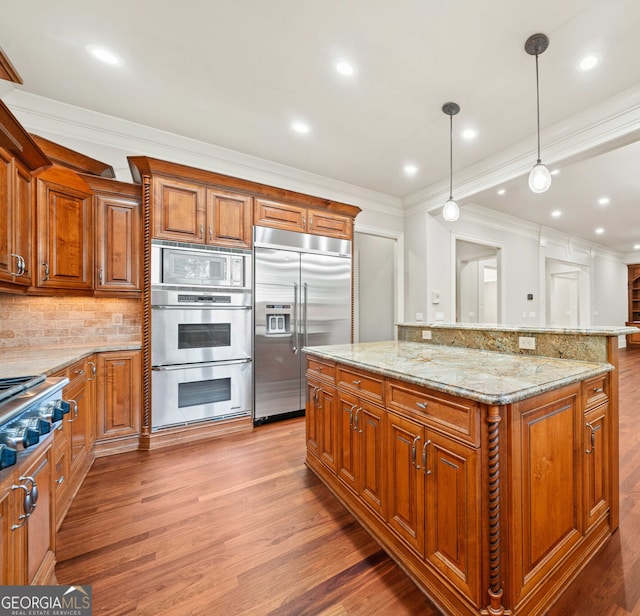 kitchen with light stone counters, brown cabinetry, wood finished floors, and built in appliances