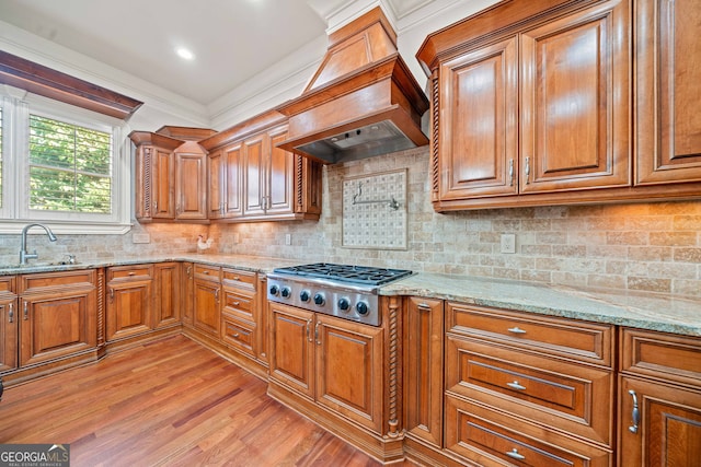 kitchen with brown cabinetry, premium range hood, stainless steel gas stovetop, and a sink