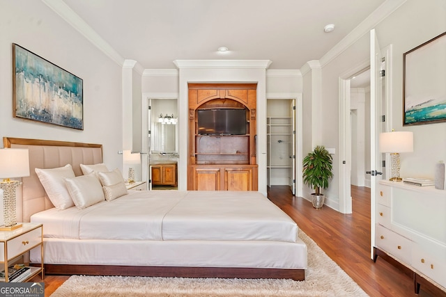 bedroom with baseboards, ornamental molding, wood finished floors, and connected bathroom