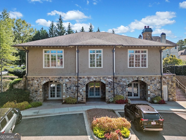 view of front of home featuring stone siding, french doors, roof with shingles, stairway, and a chimney