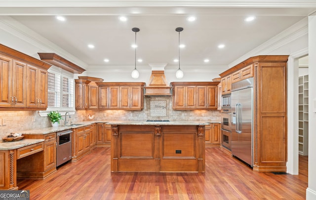 kitchen with a kitchen island, ornamental molding, built in appliances, custom exhaust hood, and a sink