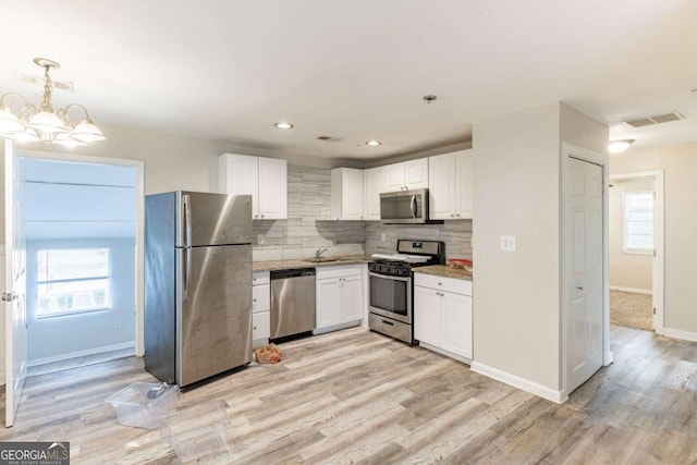 kitchen with stainless steel appliances, a sink, visible vents, white cabinets, and tasteful backsplash