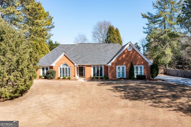 view of front of house featuring fence, brick siding, and roof with shingles