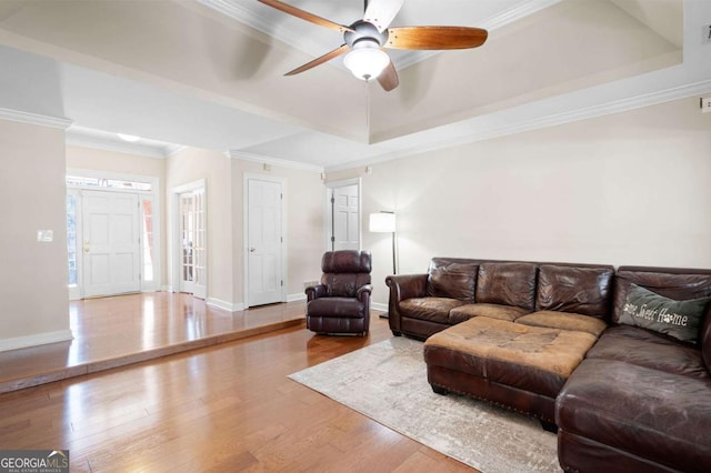 living room featuring a raised ceiling, ornamental molding, a ceiling fan, wood finished floors, and baseboards