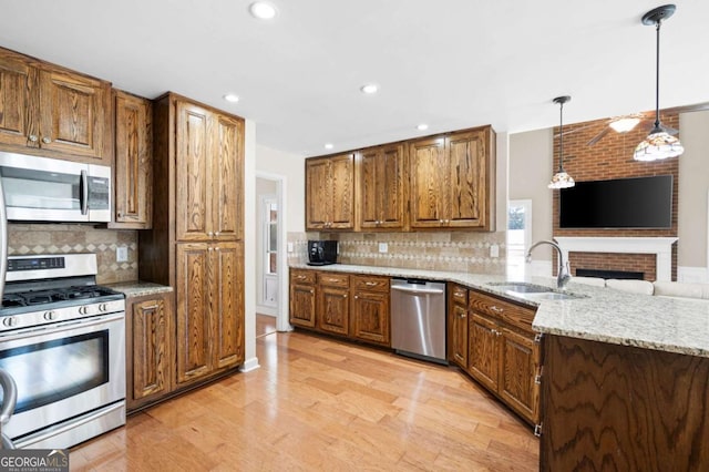 kitchen featuring light stone counters, brown cabinetry, a sink, appliances with stainless steel finishes, and light wood-type flooring