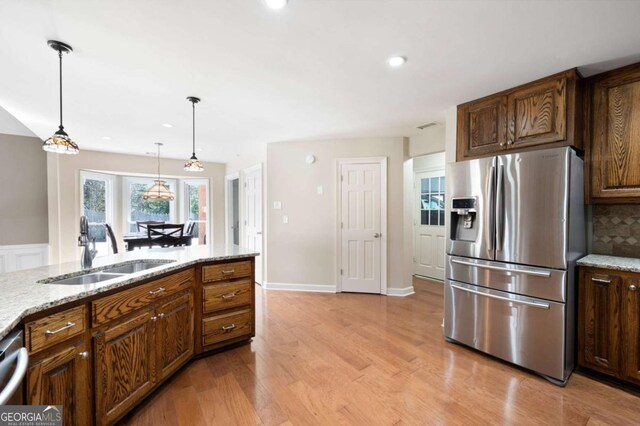 kitchen featuring light wood-style flooring, a sink, light stone counters, backsplash, and stainless steel appliances