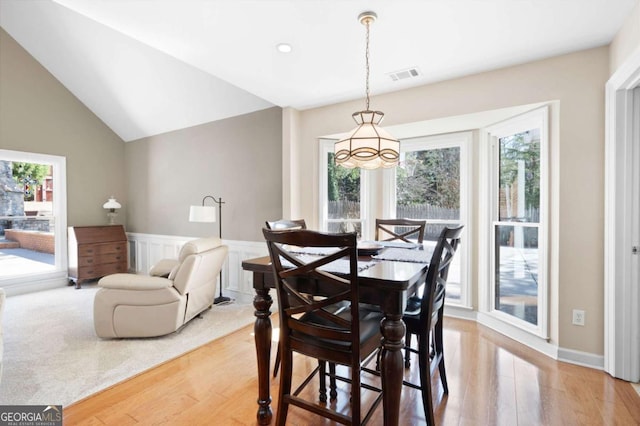 dining space with light wood finished floors, a wainscoted wall, lofted ceiling, and visible vents