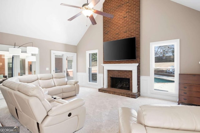 living room featuring a wainscoted wall, carpet flooring, a fireplace, high vaulted ceiling, and a ceiling fan