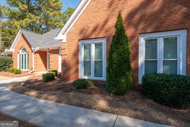 view of property exterior featuring brick siding and a shingled roof