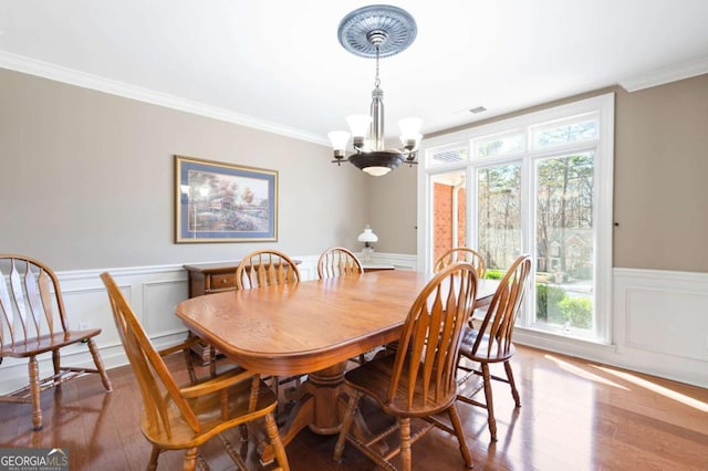 dining room featuring visible vents, a notable chandelier, hardwood / wood-style floors, wainscoting, and crown molding