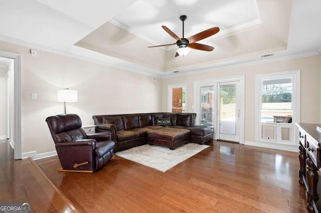 living room featuring visible vents, baseboards, ornamental molding, wood finished floors, and a raised ceiling