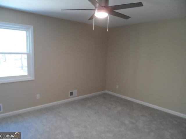 carpeted empty room with baseboards, visible vents, and a ceiling fan