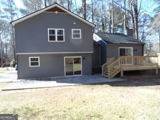 rear view of property with a lawn, a chimney, a wooden deck, and a patio