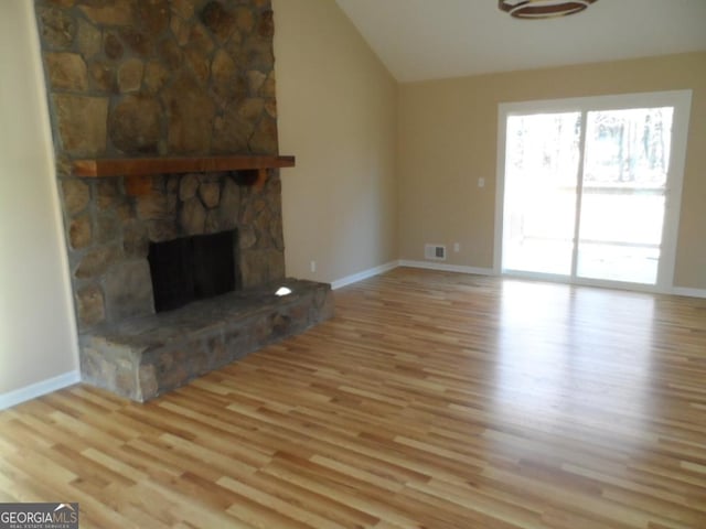 unfurnished living room featuring lofted ceiling, a stone fireplace, wood finished floors, visible vents, and baseboards