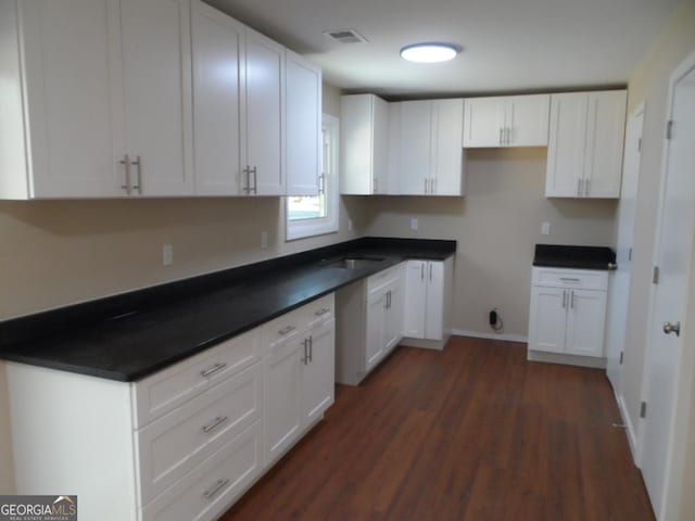 kitchen featuring visible vents, dark wood-type flooring, dark countertops, and white cabinetry