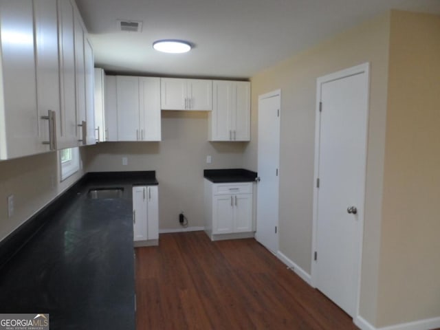 kitchen featuring baseboards, visible vents, dark countertops, dark wood-type flooring, and white cabinetry