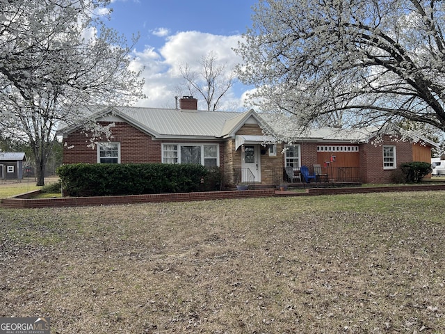 ranch-style home featuring metal roof, a front yard, brick siding, and a chimney